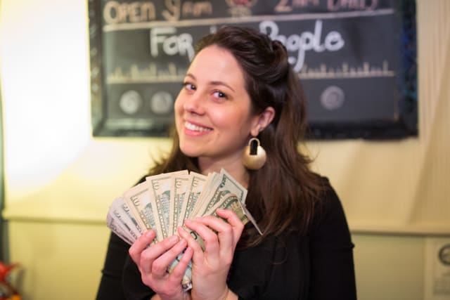 Woman smiling and holding a fan of cash, celebrating fundraising efforts for My Voice Music at the Love Bomb 2017 event organized by Murmur Creative.